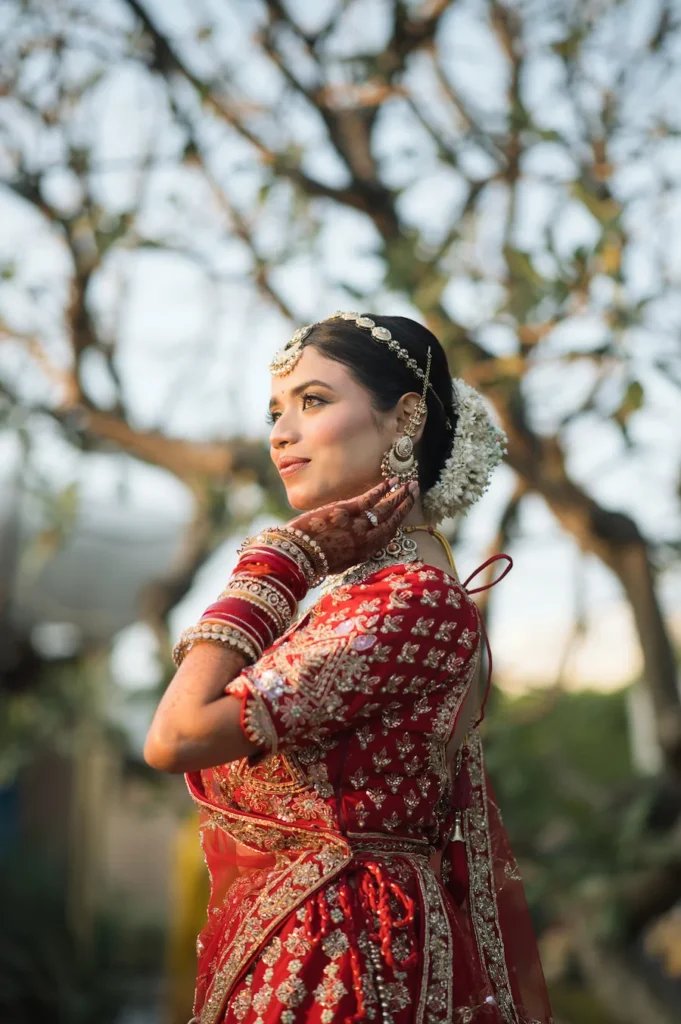Graceful bridal portrait featuring traditional red bridal attire, floral hair bun, and elegant bridal jewelry in natural light.