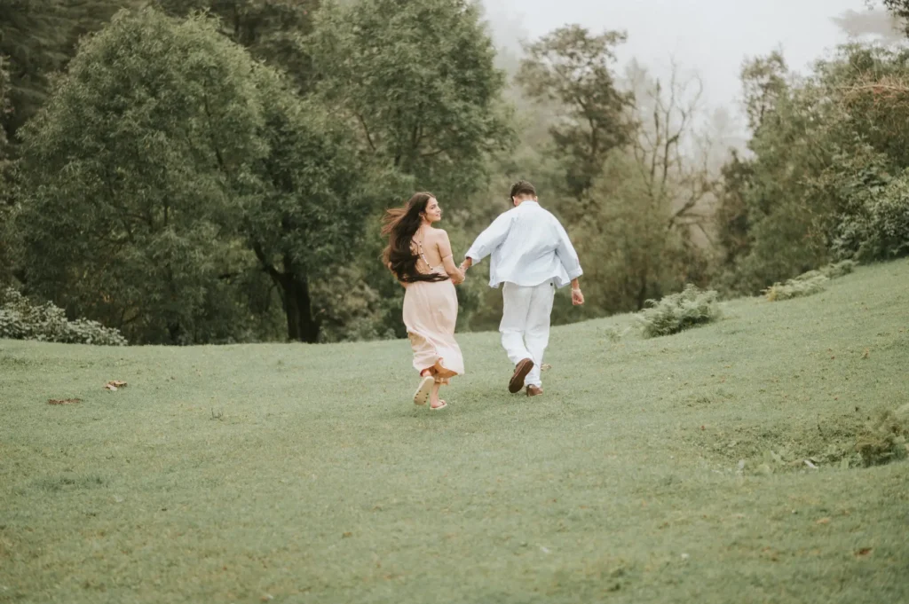 Couple walking hand in hand across a lush green meadow surrounded by peaceful forest scenery