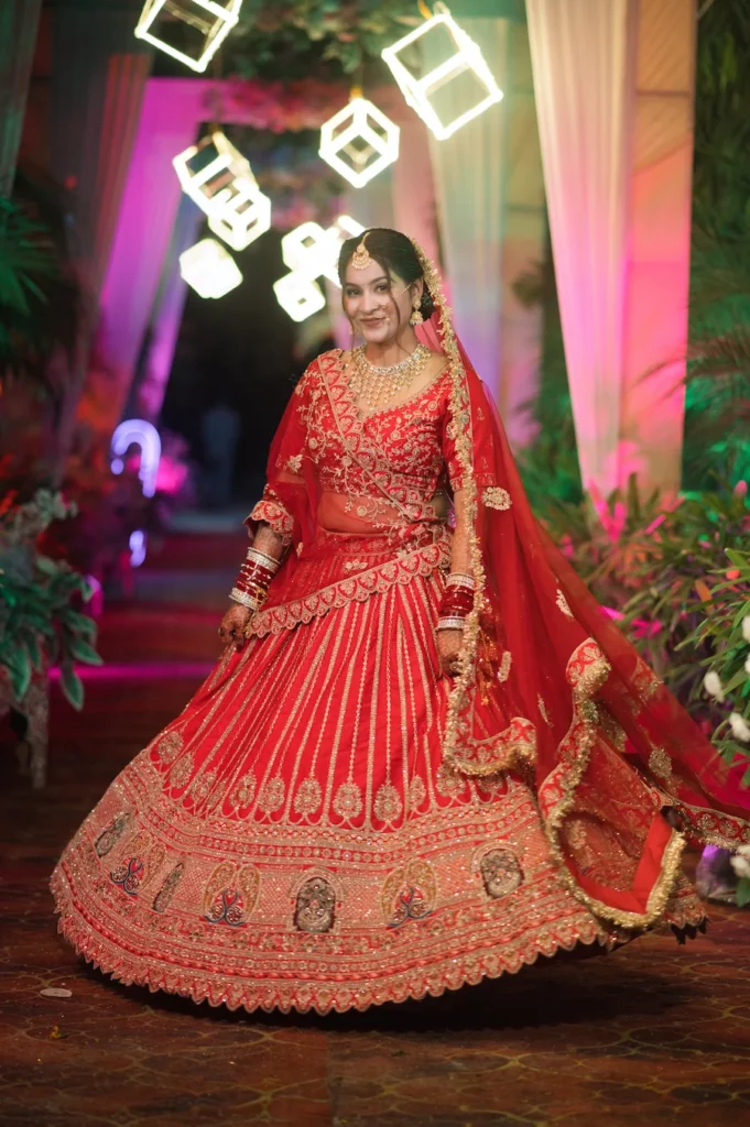 Bride twirling in a red bridal lehenga during a joyful wedding celebration.