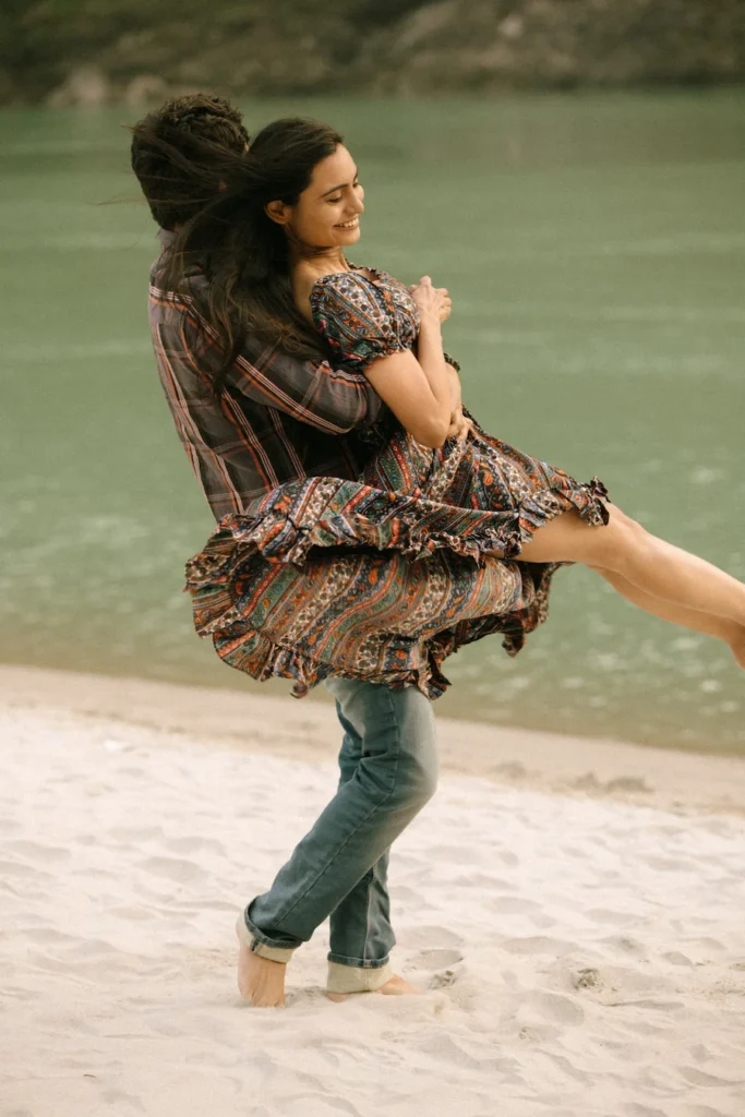 Groom lifting the bride on a sandy riverbank during a joyful outdoor couple photoshoot