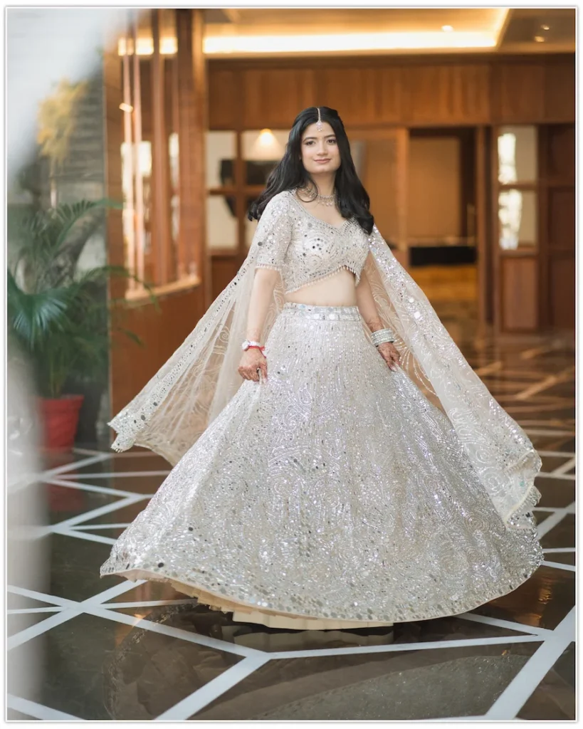 Graceful bride twirling in a sparkling silver lehenga with natural light and elegant indoor setting.