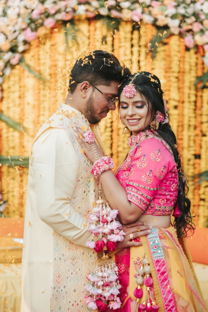 Couple sharing a romantic embrace during a colorful haldi ceremony with floral décor and joyful wedding celebrations.