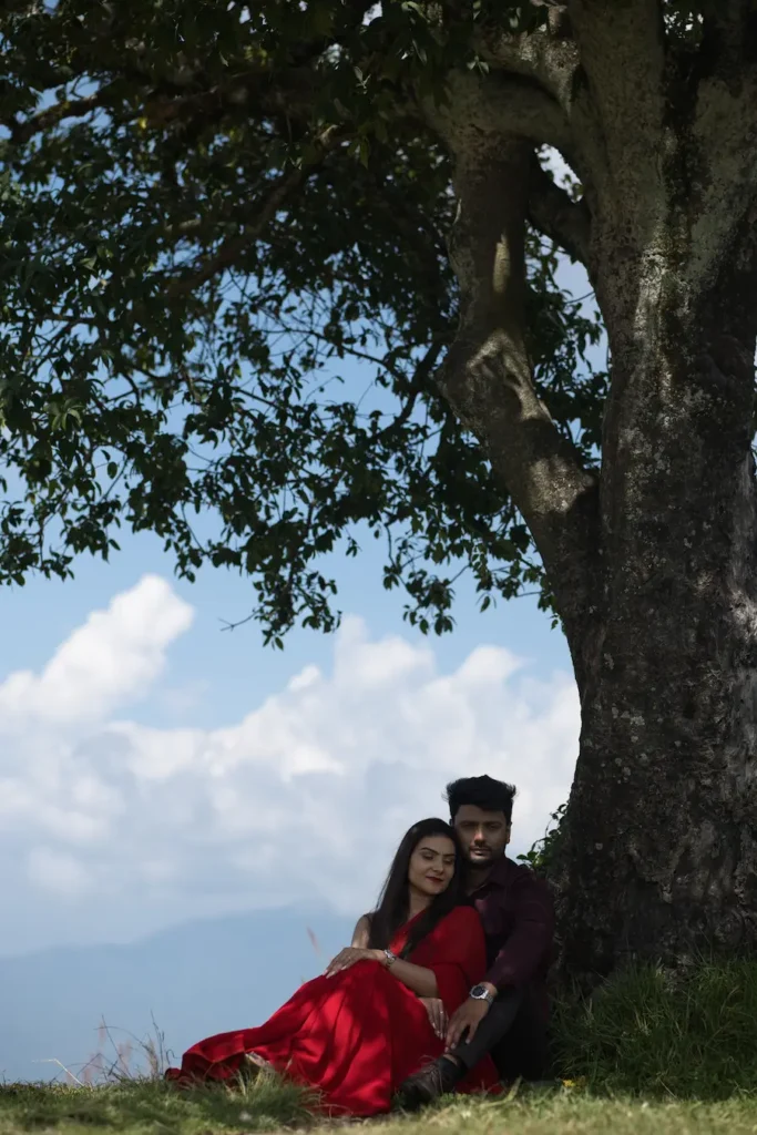 Couple resting under a large tree with scenic mountain views in the background.