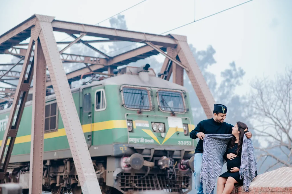 Creative maternity shoot in Dehradun with an expecting couple posing beside a train bridge during golden hour