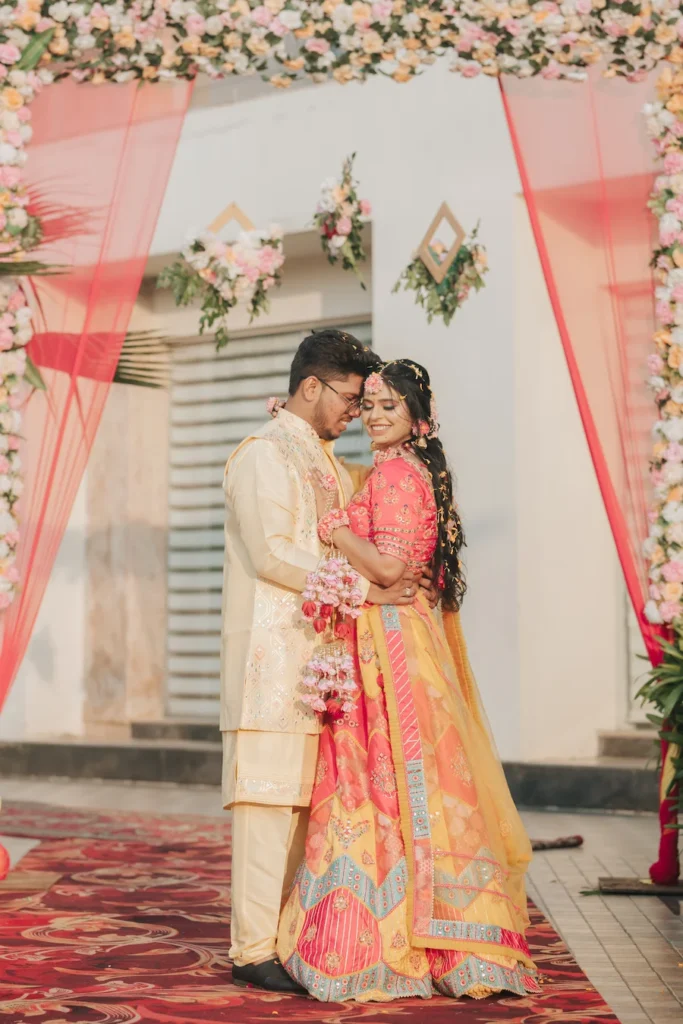 Bride and groom posing beneath a beautifully decorated floral entrance during their wedding celebration.