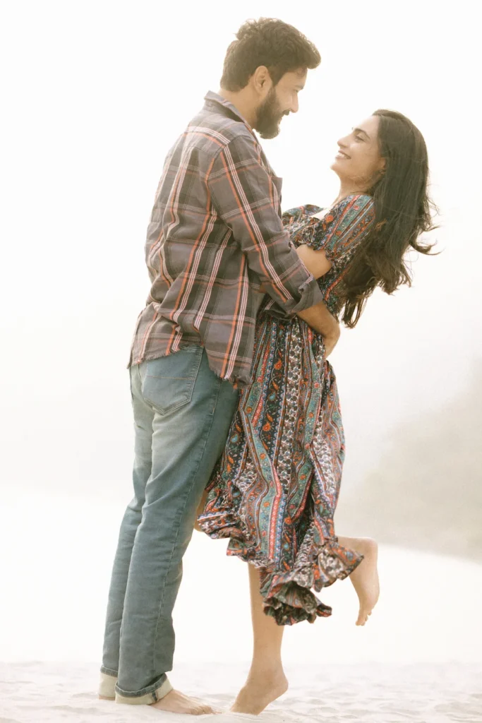 Romantic couple sharing a joyful embrace on a sandy riverside during a natural outdoor photoshoot