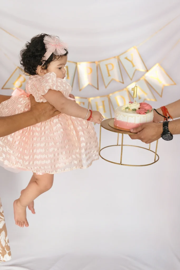 Baby reaching toward a birthday cake during a first birthday celebration