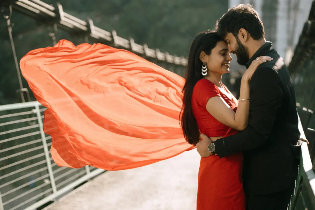 Romantic couple embracing on a suspension bridge with a flowing red dress creating a dramatic and cinematic scene