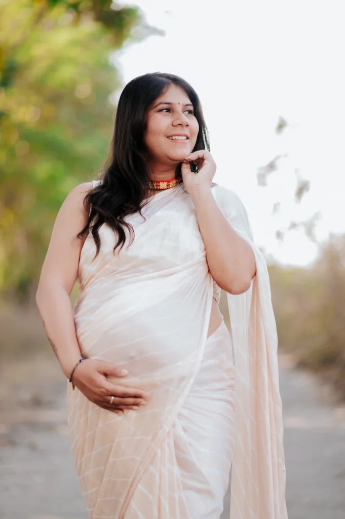 Elegant outdoor portrait of an expecting mother in a white saree surrounded by natural light