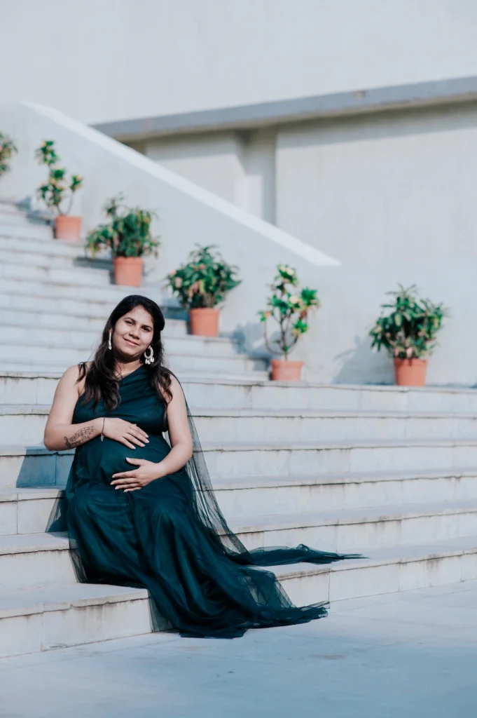 Expecting mother sitting on white stairs in a flowing gown during a lifestyle pregnancy photoshoot