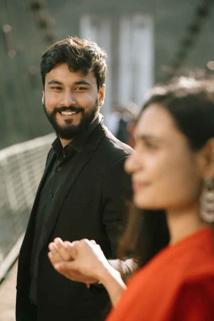 Smiling groom looking lovingly at his partner while holding hands on a suspension bridge