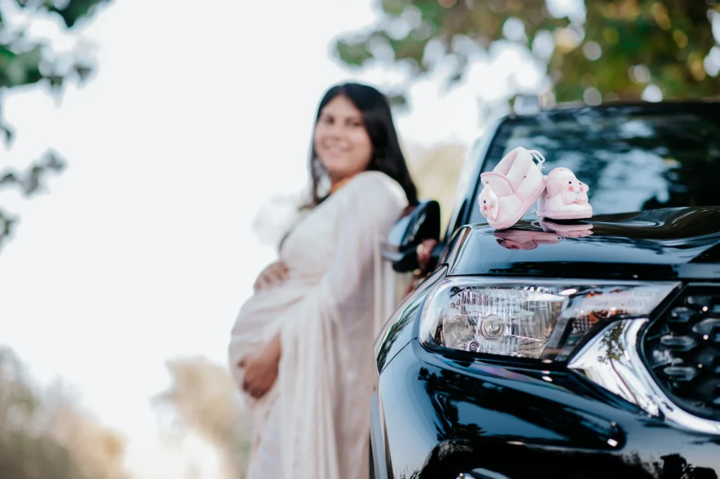 Baby shoes placed on a car bonnet beside an expecting mother, symbolizing the arrival of a new family member