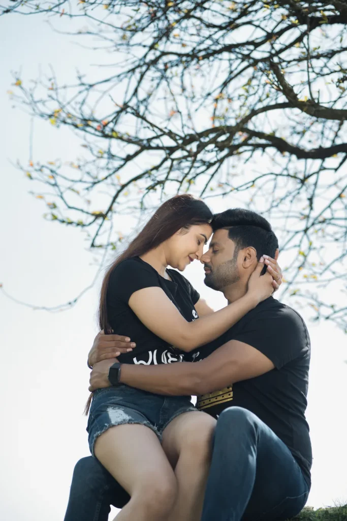 Couple sharing a romantic moment under a tree beside a scenic hillside.