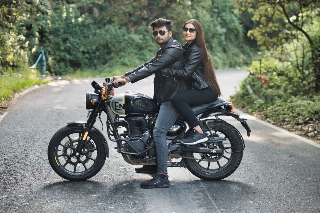 Stylish couple posing together on a motorcycle along a scenic forest road.