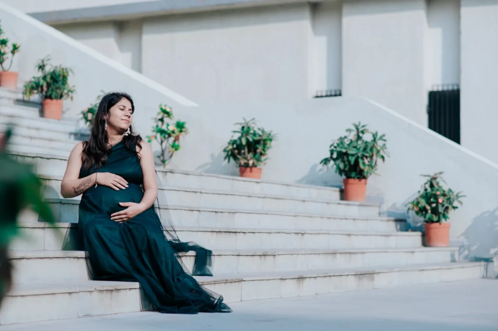 Expecting mother relaxing on white stairs in an elegant gown during an outdoor portrait session