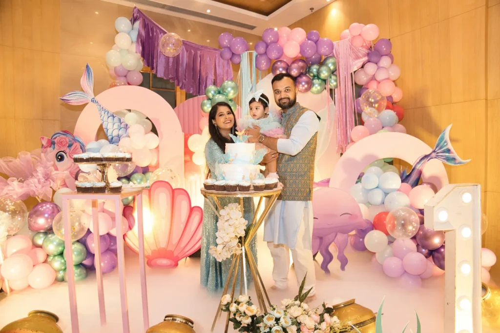 Family posing together in front of a colorful first birthday party decoration