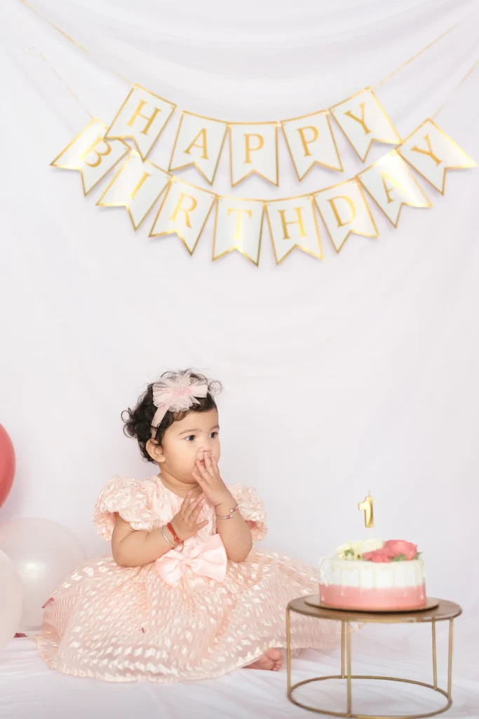 Toddler sitting beside a birthday cake with a Happy Birthday backdrop