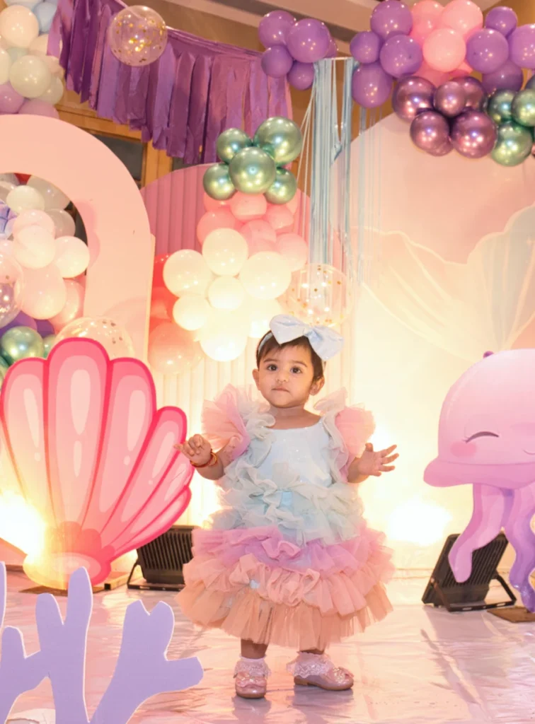 Toddler in a pastel ruffle dress standing on a colorful birthday party stage