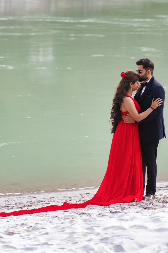 Couple sharing an intimate moment on a sandy riverbank in elegant pre-wedding outfits