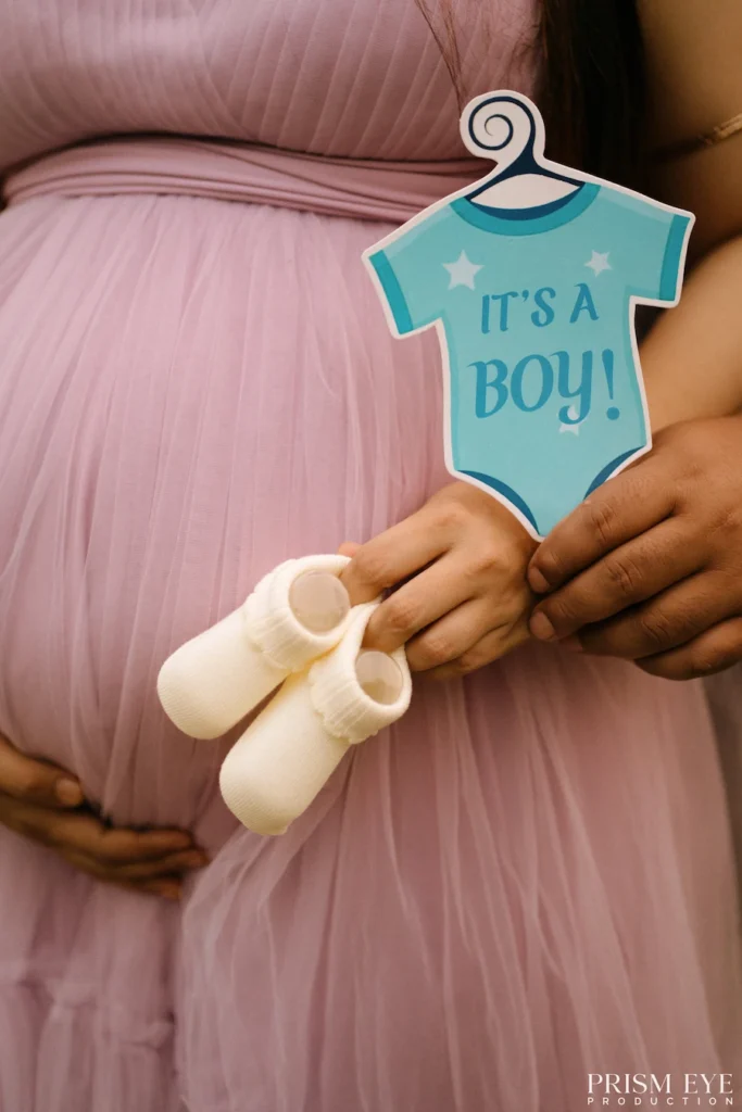 Close-up of baby shoes and a blue baby announcement sign held over an expecting mother's baby bump.