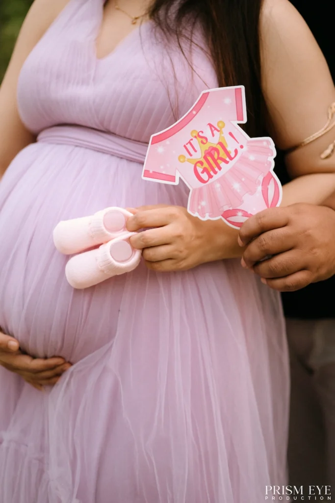 Pink baby announcement sign and tiny baby shoes displayed over an expecting mother's baby bump.