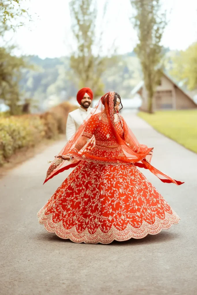 Bride twirling gracefully in a red bridal lehenga during an outdoor wedding photoshoot.