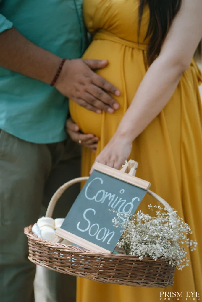 Expecting couple holding a decorative basket with a coming soon sign during an outdoor maternity shoot.