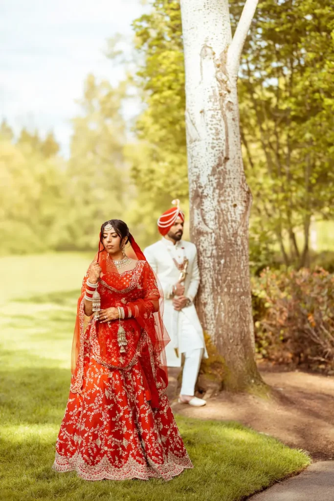 Creative wedding portrait of the bride in the foreground with the groom waiting beside a tree.