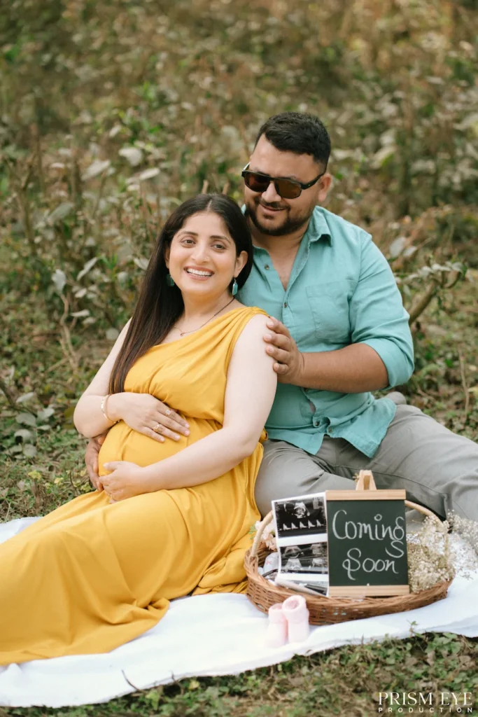 Expecting couple smiling together with baby announcement props during a relaxed outdoor portrait.