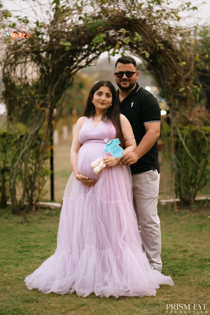 Parents-to-be posing beneath a garden arch while celebrating their pregnancy together.
