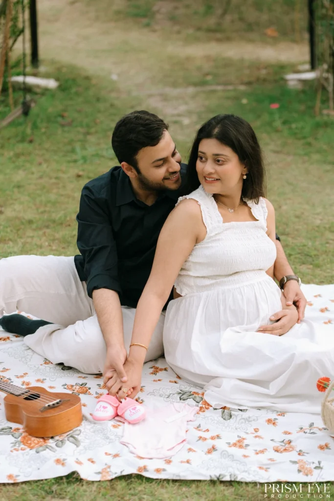 Expecting parents enjoying a romantic picnic during a maternity photoshoot in a garden.