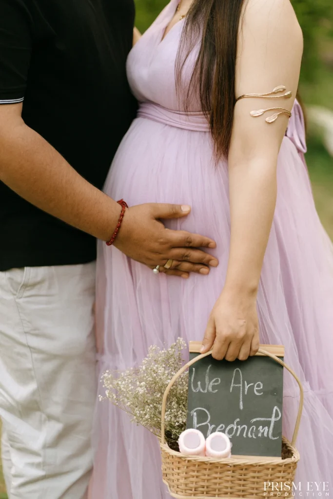 Close-up of a baby bump beside a decorative basket filled with pregnancy announcement accessories.