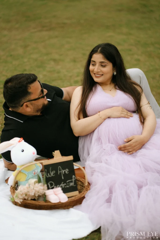 Expecting couple sharing a joyful moment on a picnic blanket surrounded by baby announcement decorations.
