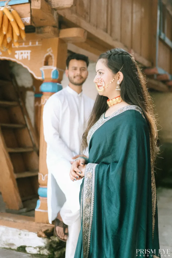 Bride looking away while the groom smiles in the background inside a traditional Uttarakhand village home
