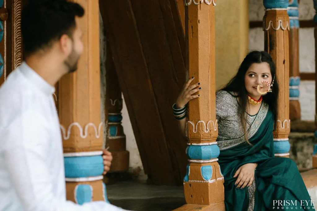 Bride peeking from behind a wooden pillar as the groom smiles across the courtyard of a heritage village home