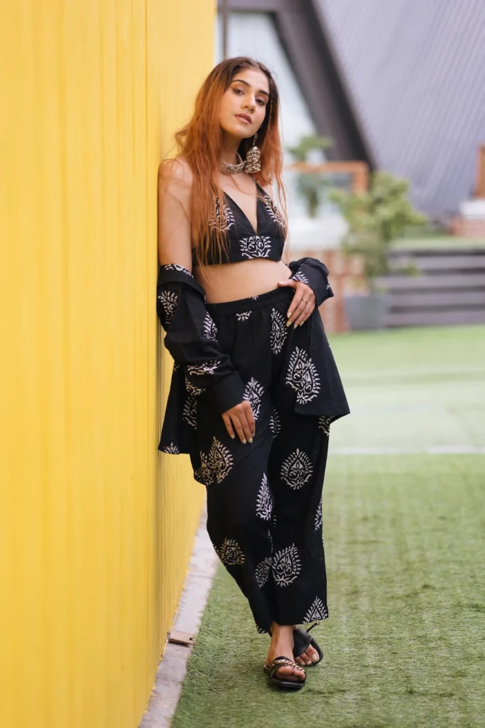 Full-length fashion portrait of a woman walking beside a vibrant yellow wall in a stylish ethnic outfit.
