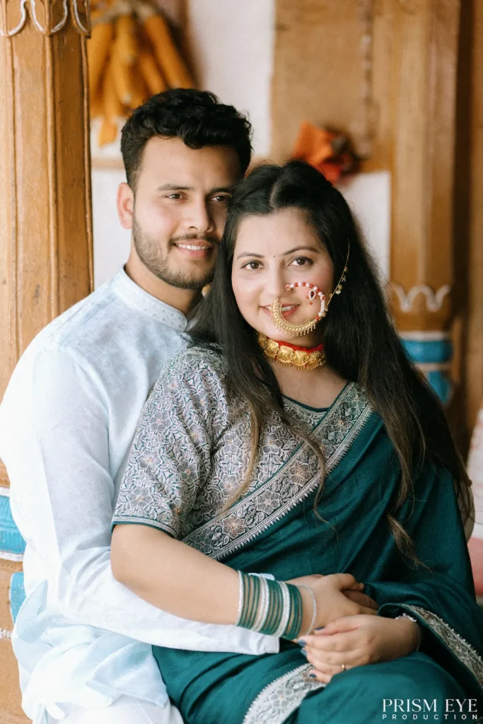 Happy couple posing together in front of beautifully carved wooden pillars and a traditional village home
