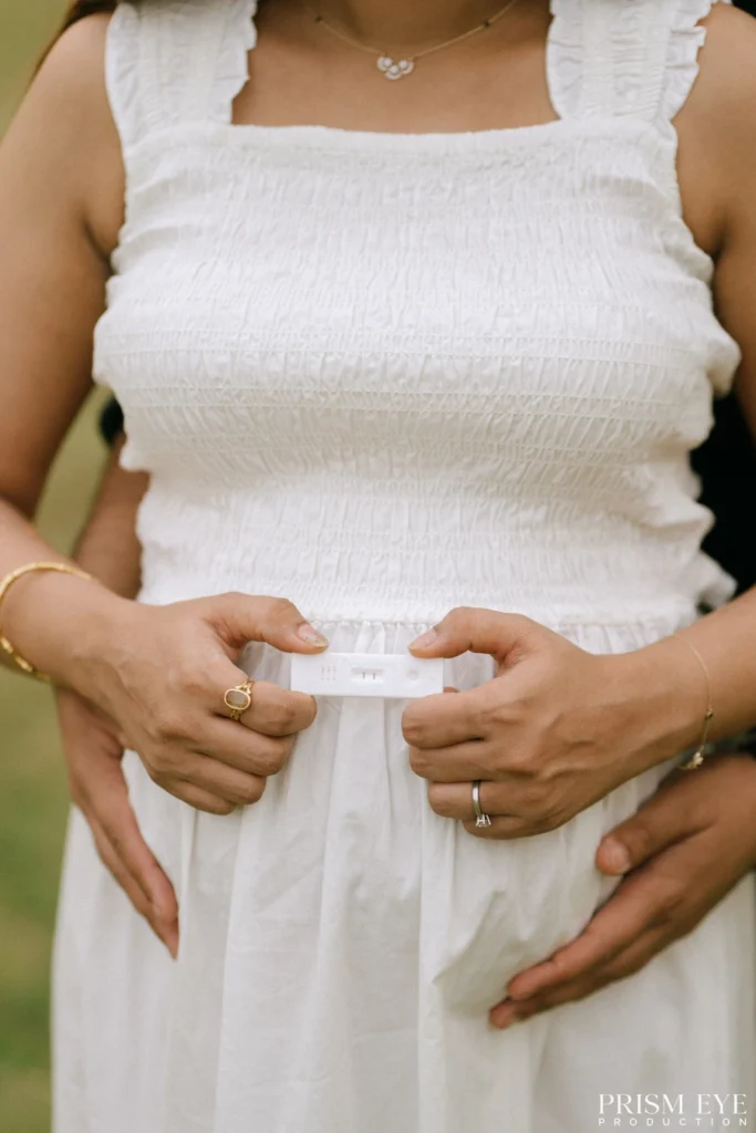 Close-up of an expecting mother holding a positive pregnancy test with her partner embracing her.