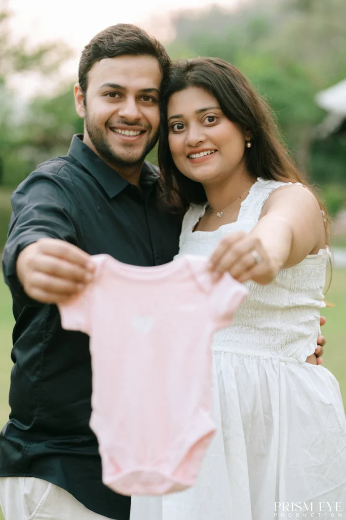 Parents-to-be proudly holding a newborn onesie while sharing joyful smiles together.