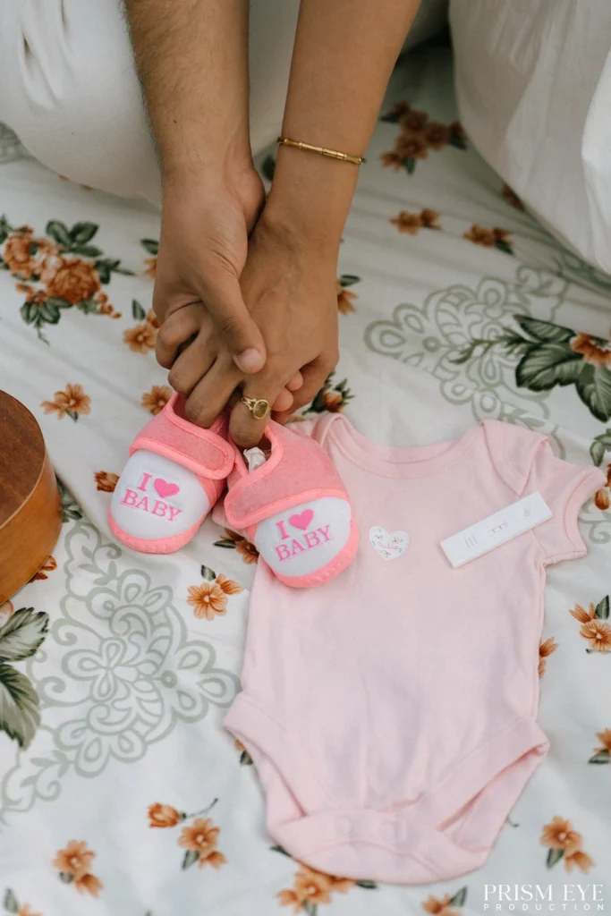 Maternity Photoshoot flat lay featuring newborn clothes, baby shoes, and pregnancy essentials to celebrate the journey into motherhood.
