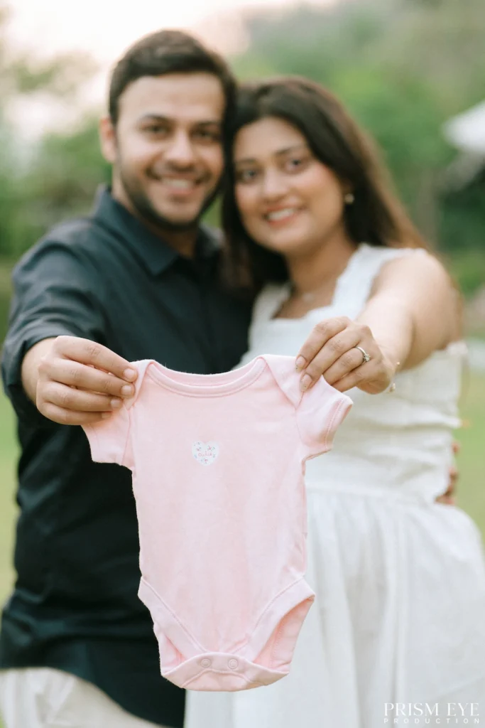 Parents proudly holding a pink newborn onesie to celebrate their growing family.