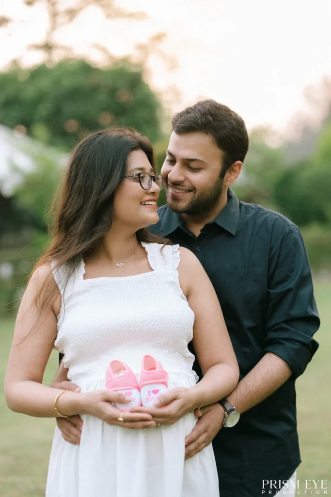 Expecting mother holding tiny baby shoes while sharing a joyful moment with her partner.