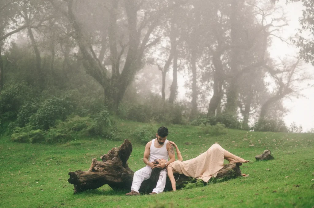 Couple relaxing on a fallen tree in a misty forest surrounded by lush greenery during a romantic outdoor photoshoot