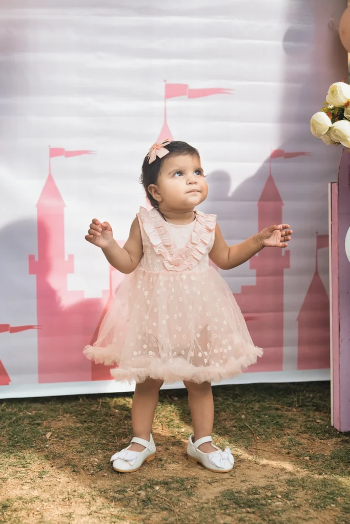 Little girl in a pink birthday dress posing in front of a themed first birthday backdrop.