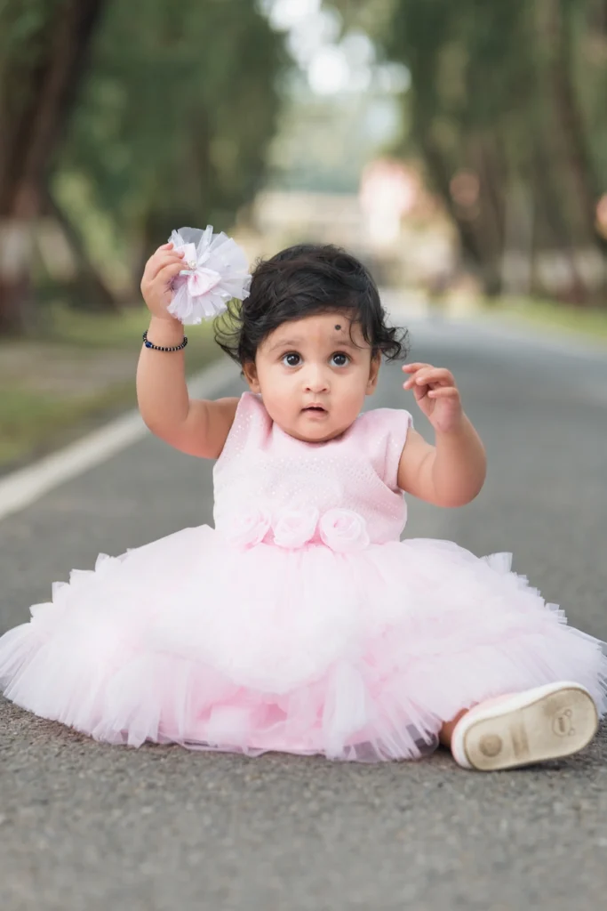 Cute baby sitting on a quiet road wearing a fluffy pink dress and floral headband.