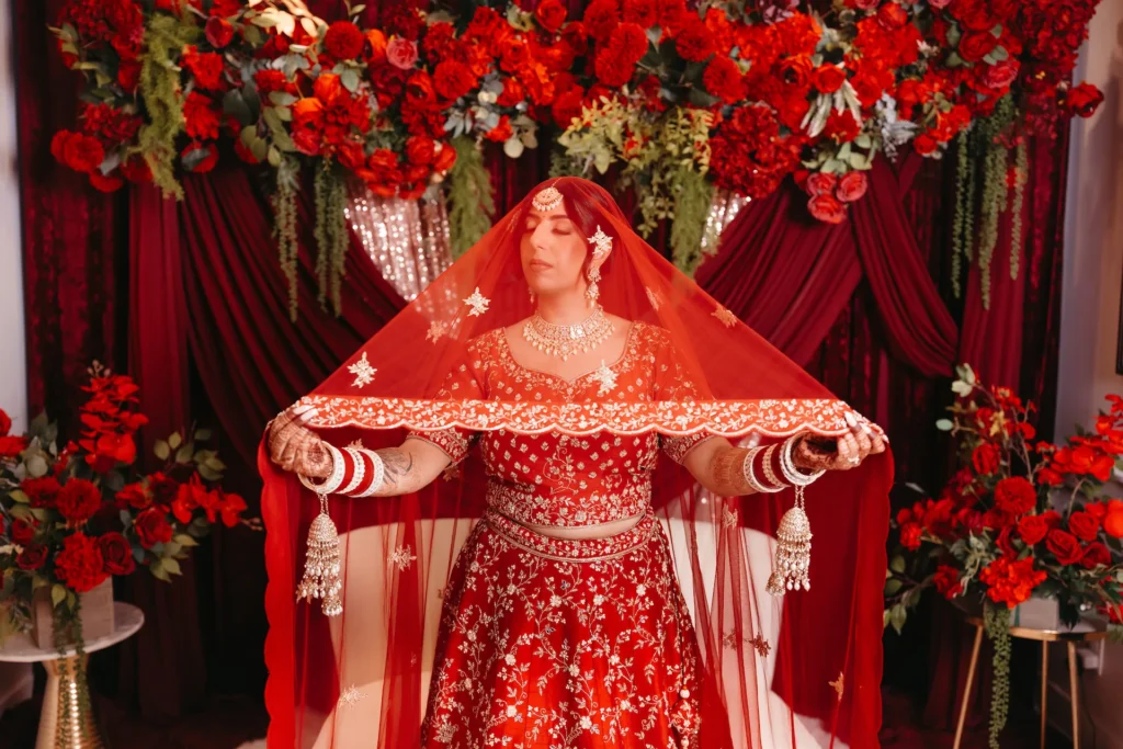 Bride under red dupatta during a Punjabi Wedding in Rishikesh with elegant floral decor and traditional bridal attire