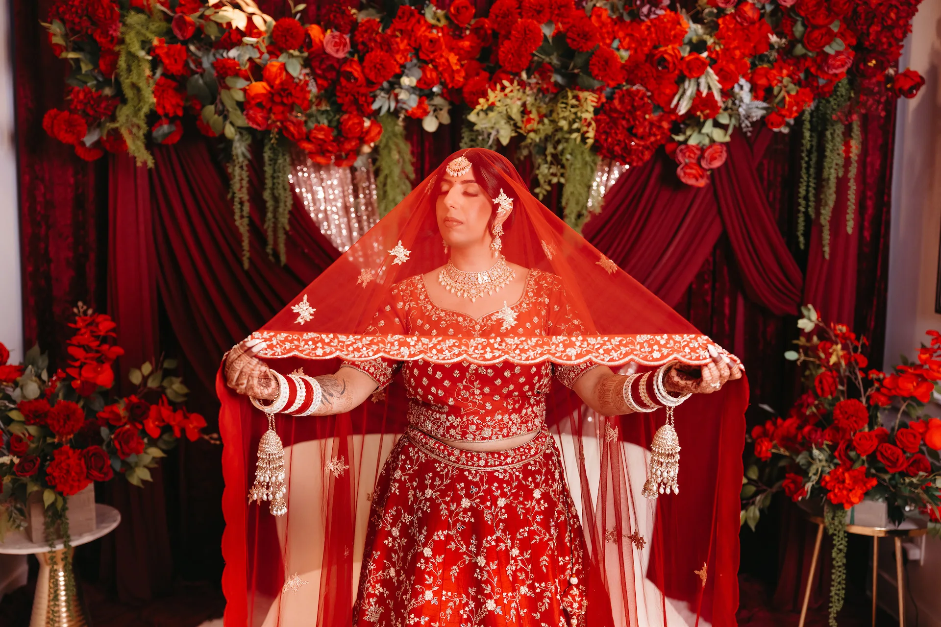 Bride under red dupatta during a Punjabi Wedding in Rishikesh with elegant floral decor and traditional bridal attire