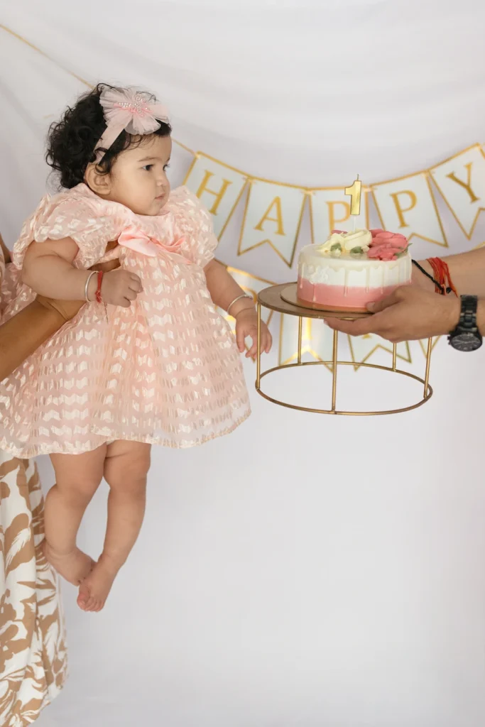 Baby girl celebrating her birthday while looking at a cake with a Happy Birthday decoration.