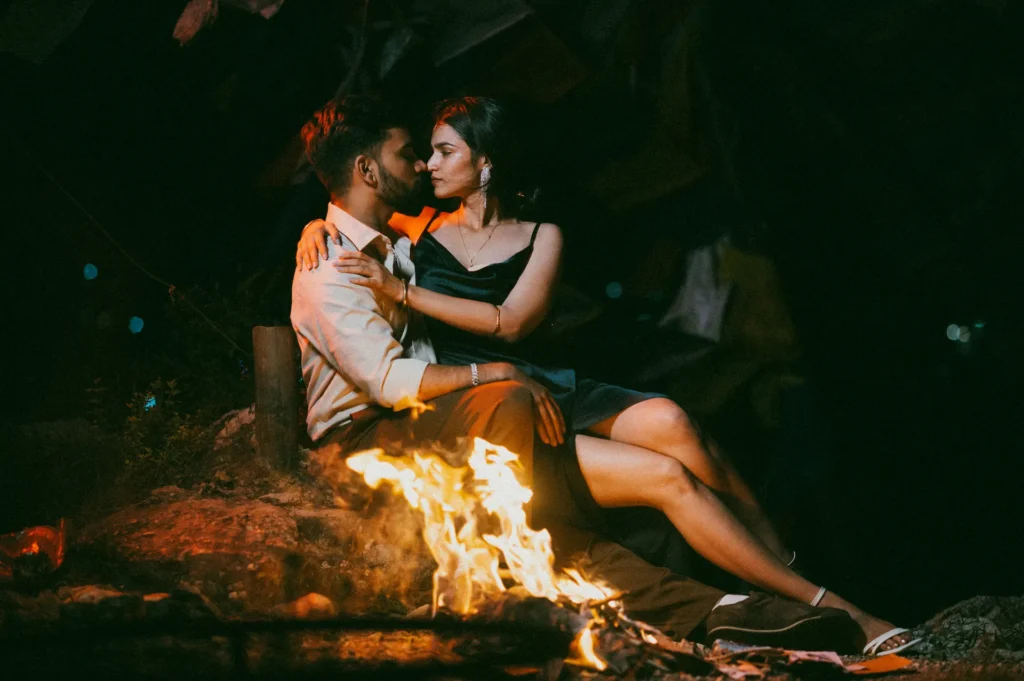 Couple embracing beside a campfire during an evening photoshoot with cinematic lighting and warm tones