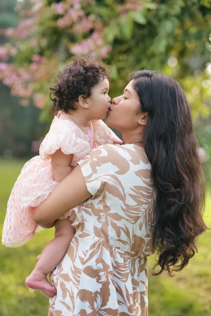 Mother holding and kissing her baby girl during a heartwarming outdoor moment.